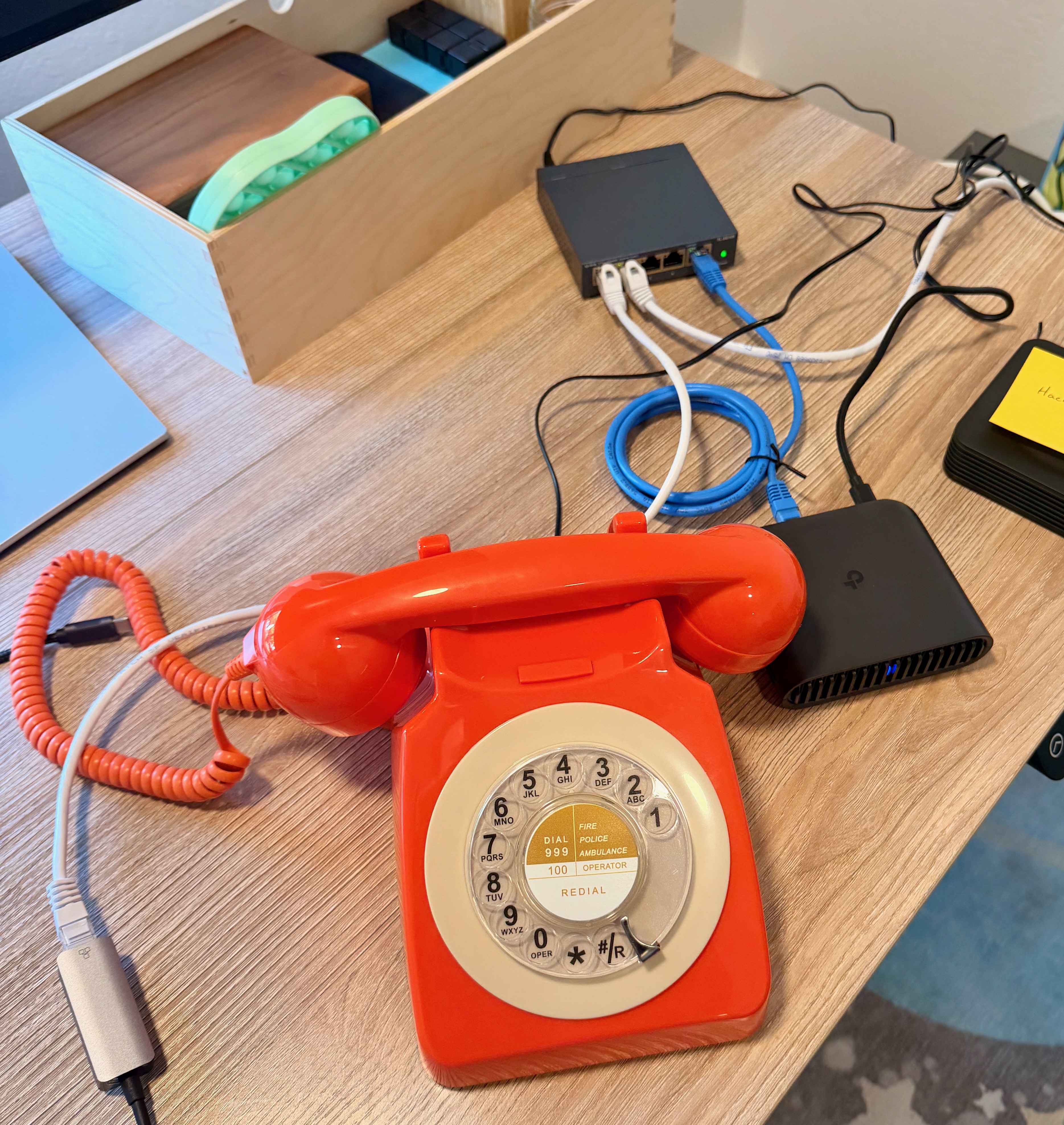 An orange rotary phone on a desk, connected to a Grandstream HT802 ATA and a TP-Link travel router